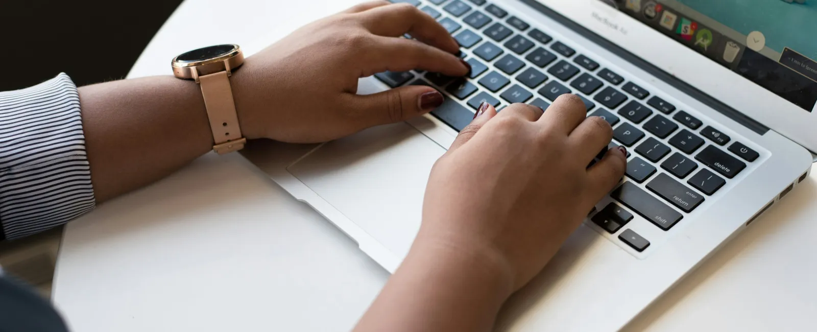 Hands typing on a silver laptop keyboard with a wristwatch on left wrist and a game on screen.