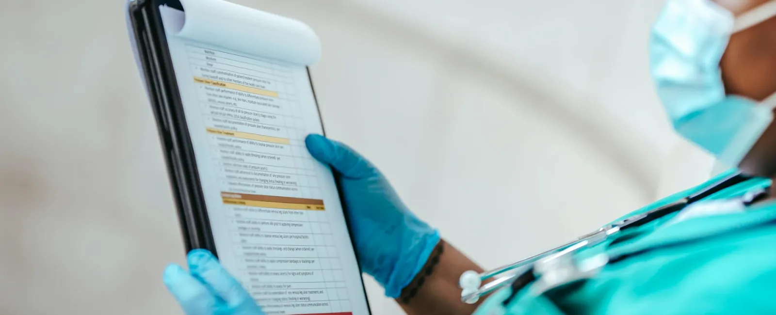 Healthcare professional in surgical gloves and mask reviewing medical checklist on clipboard.