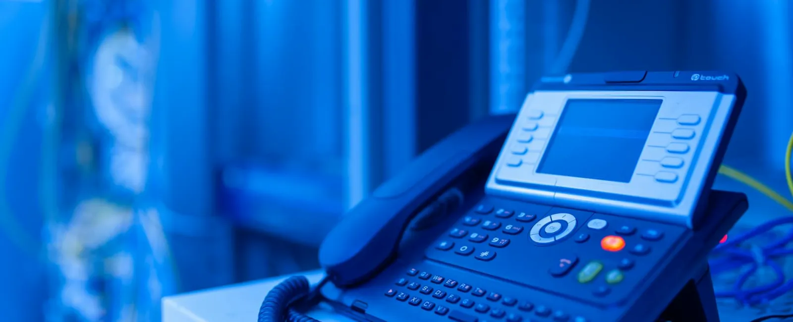 Black office desk phone with a digital screen and keypad on a white surface with blue background.