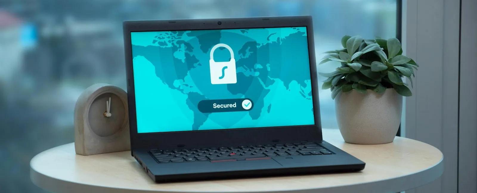 Laptop on round table showing secured network screen with lock icon and world map background.