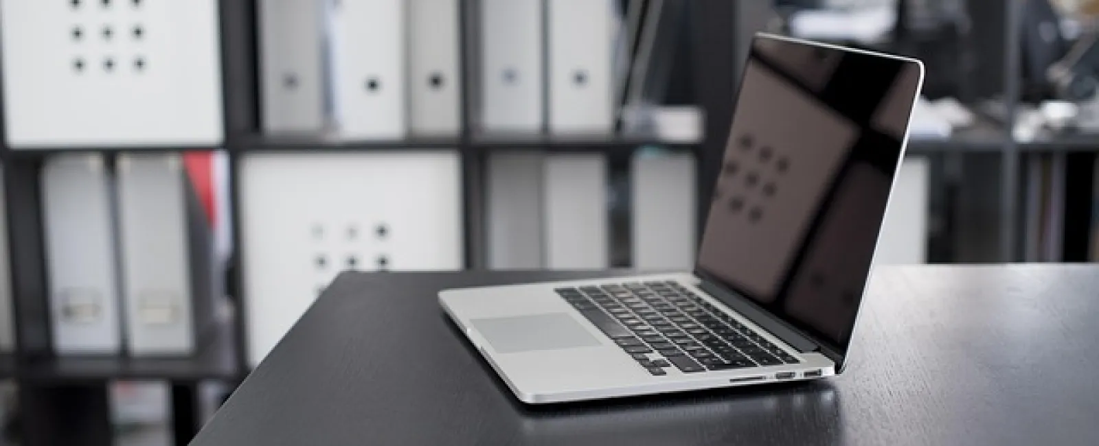 Open laptop on black office desk with blurred shelves and binders in the background