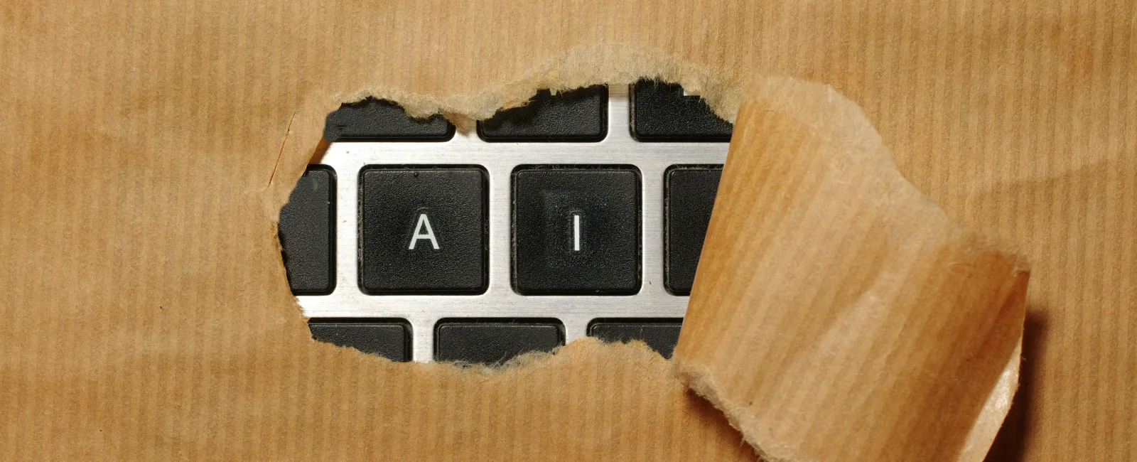 Keyboard keys A and I visible through torn brown paper symbolizing artificial intelligence concept.