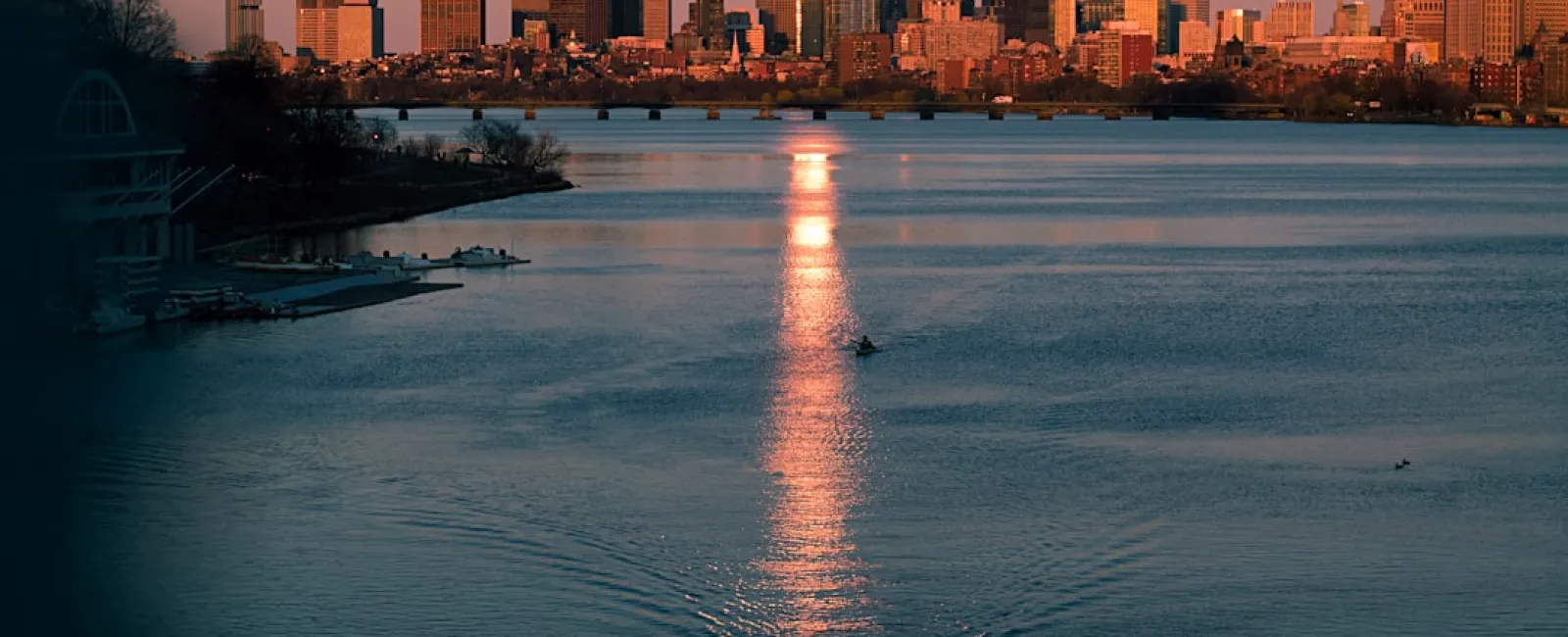 Paddleboarder on calm river at sunset with city skyline and reflections in the water