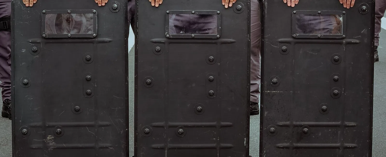 Police officers holding black riot shields in a line during a public safety operation.