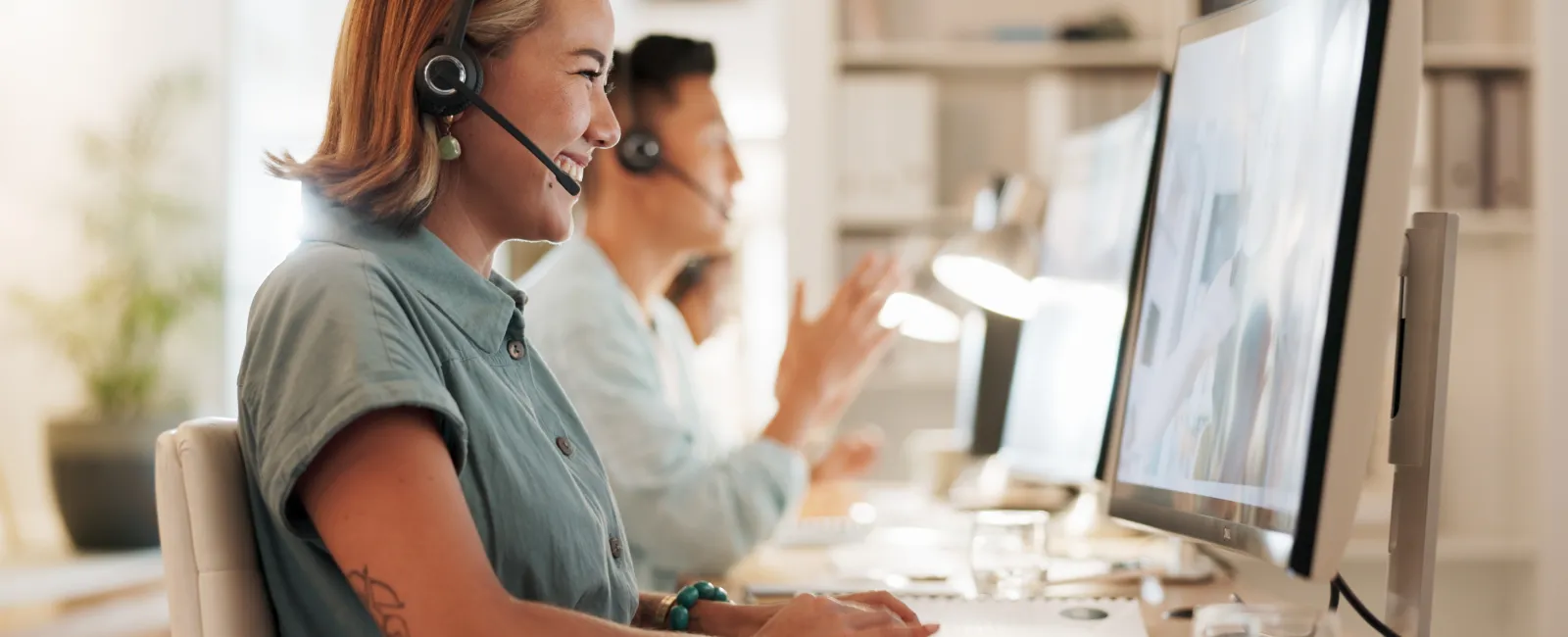 Smiling customer service representatives wearing headsets and working on computers in modern office.