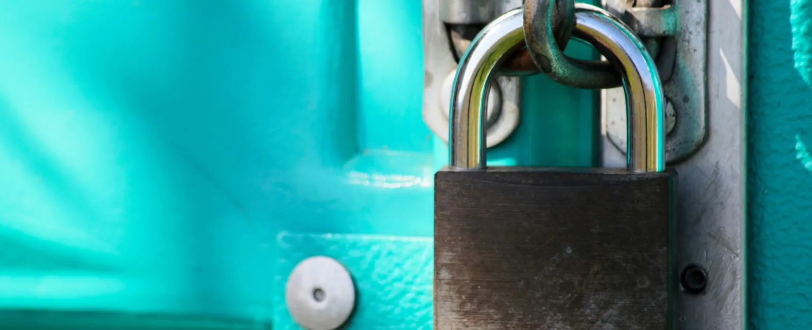 Close-up of a weathered padlock securing a turquoise metal door with a chain link.