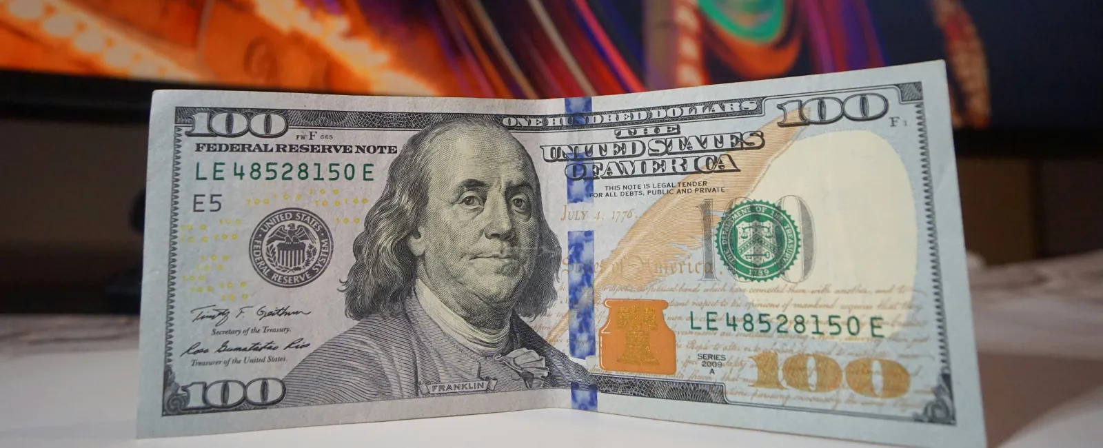 $100 bill with Colorful Background on a computer screen showcasing the financial cost of bad cybersecurity.