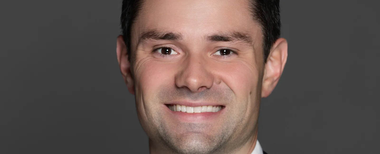Smiling man wearing navy suit and yellow tie on dark gray background professional portrait