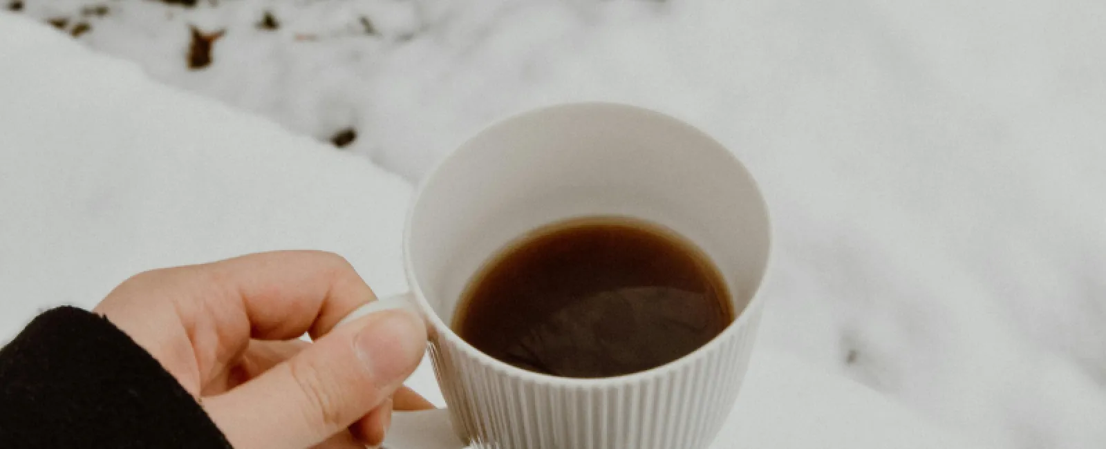 Hand holding a cup of coffee with snow-covered ground and text about winter home readiness.