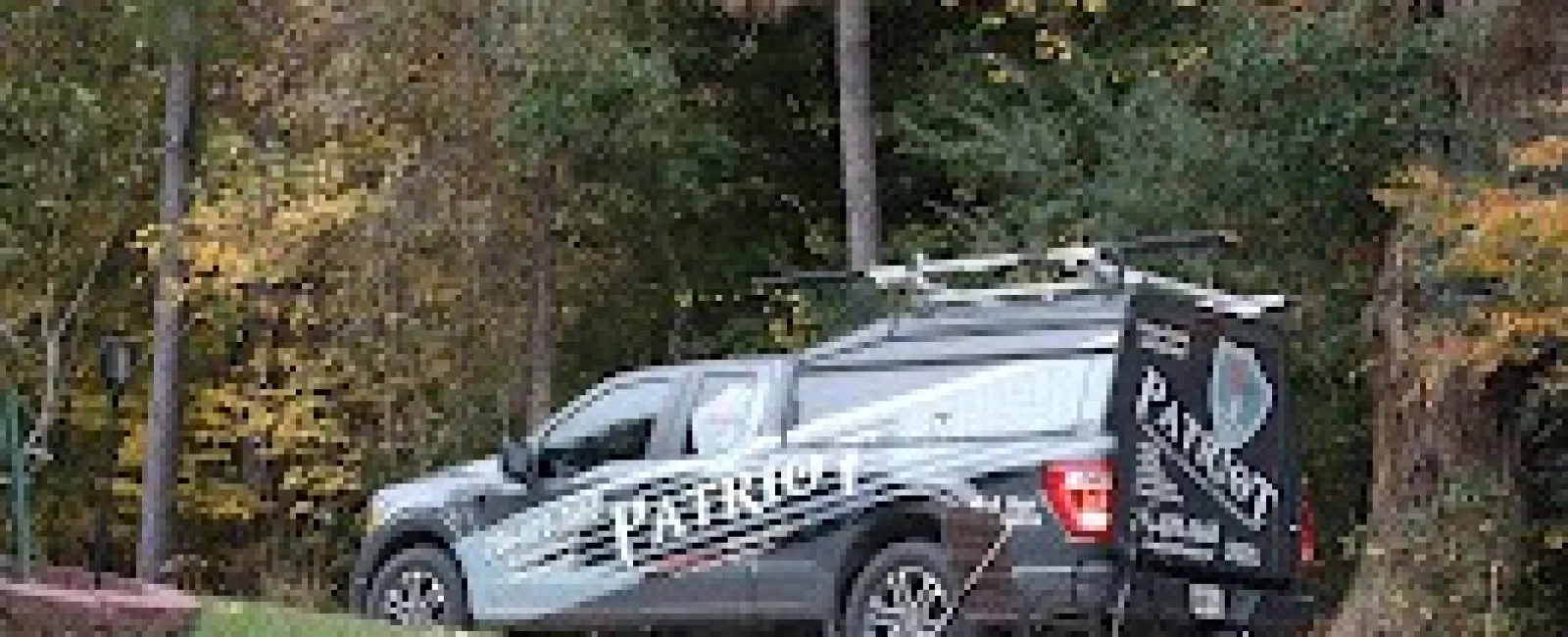 Patriot service truck parked on a grassy hill near trees and a small solar panel in autumn surroundings.
