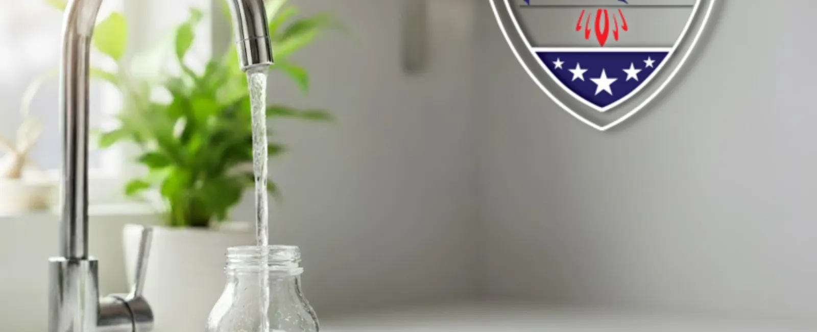 Water filling a glass bottle with a lime slice under a modern kitchen faucet with a plant in the background.