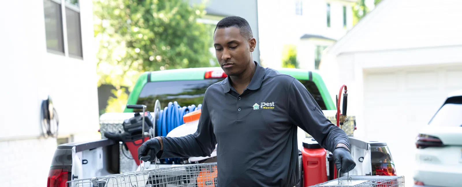 Pest control technician holding wire traps standing near green truck filled with equipment outside house.