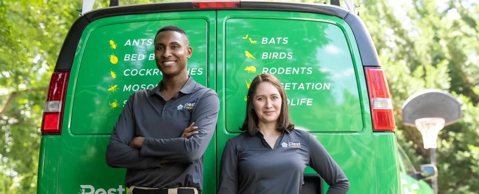 Two pest control technicians in uniform standing confidently in front of a green service van outdoors.