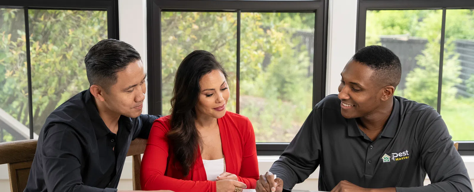 Pest control expert using tablet to explain service details to a couple at a white marble table by window.