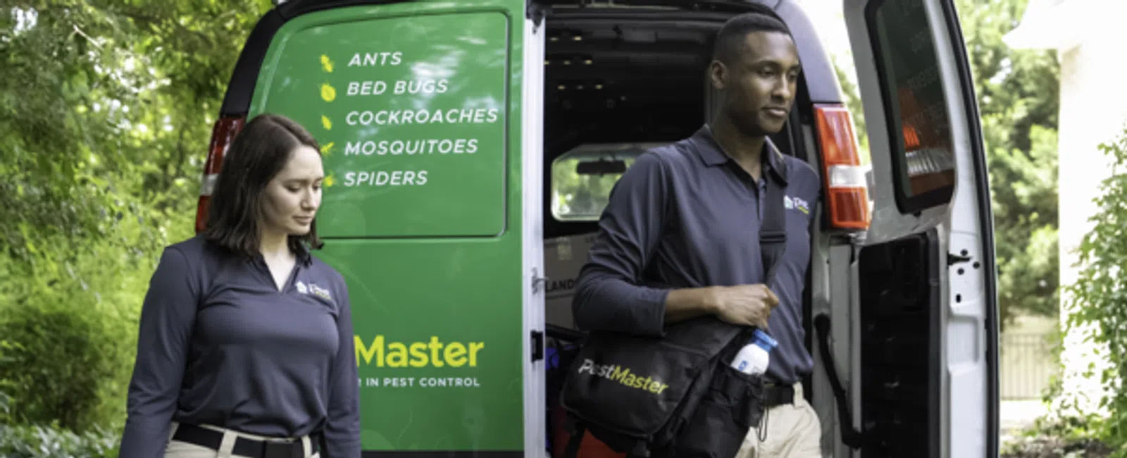 Two pest control professionals walking from a van with a list of pests serviced and equipment in hand