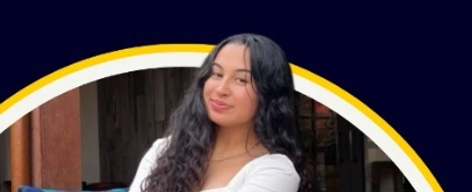 Young woman with long curly hair sitting on a chair outdoors smiling at the camera