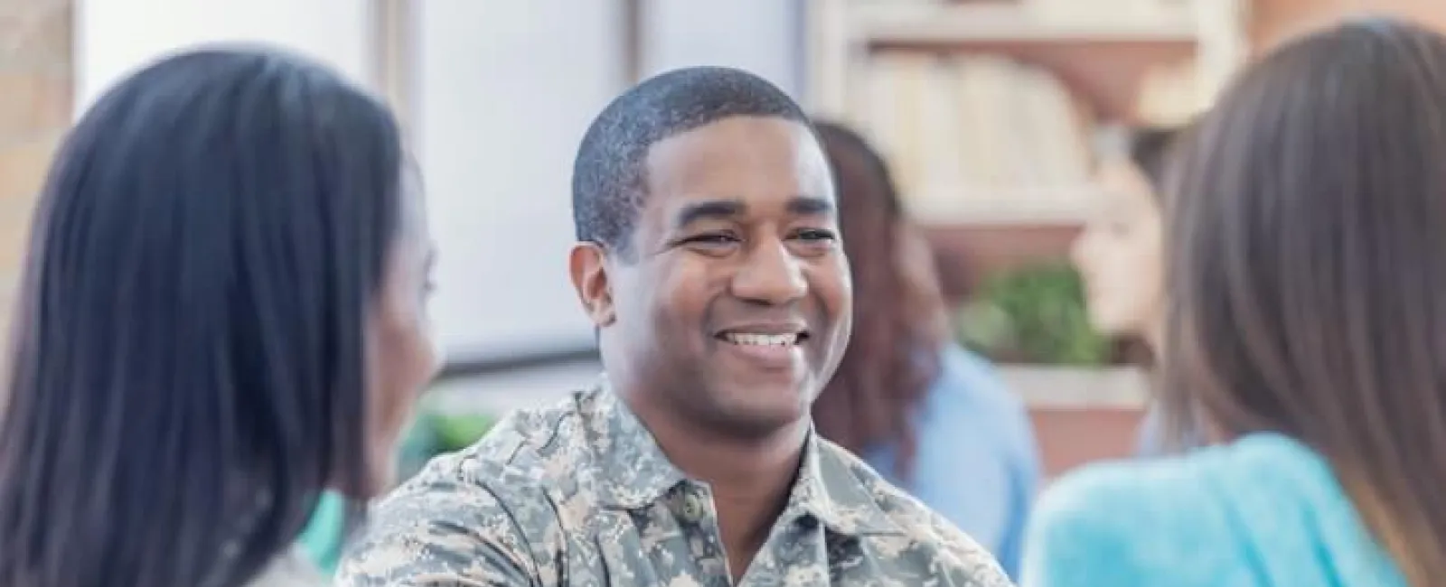 Smiling soldier in camouflage shaking hands with a woman in a friendly indoor setting.