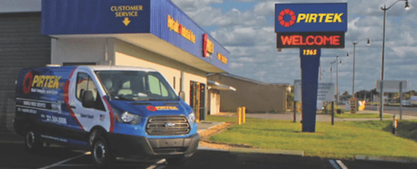 Pirtek service van parked outside customer service building with Pirtek welcome sign under blue sky with clouds