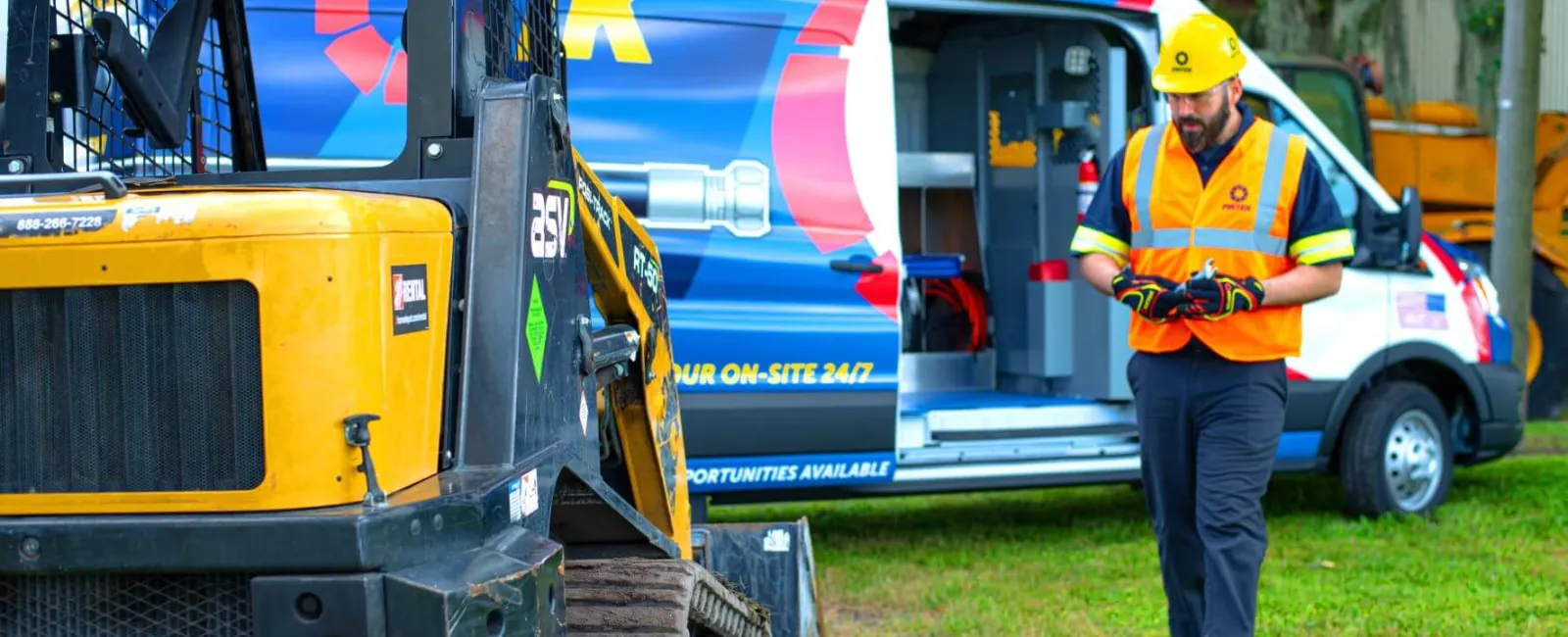Construction worker in safety gear walking on grass near equipment and a service van with open side door.