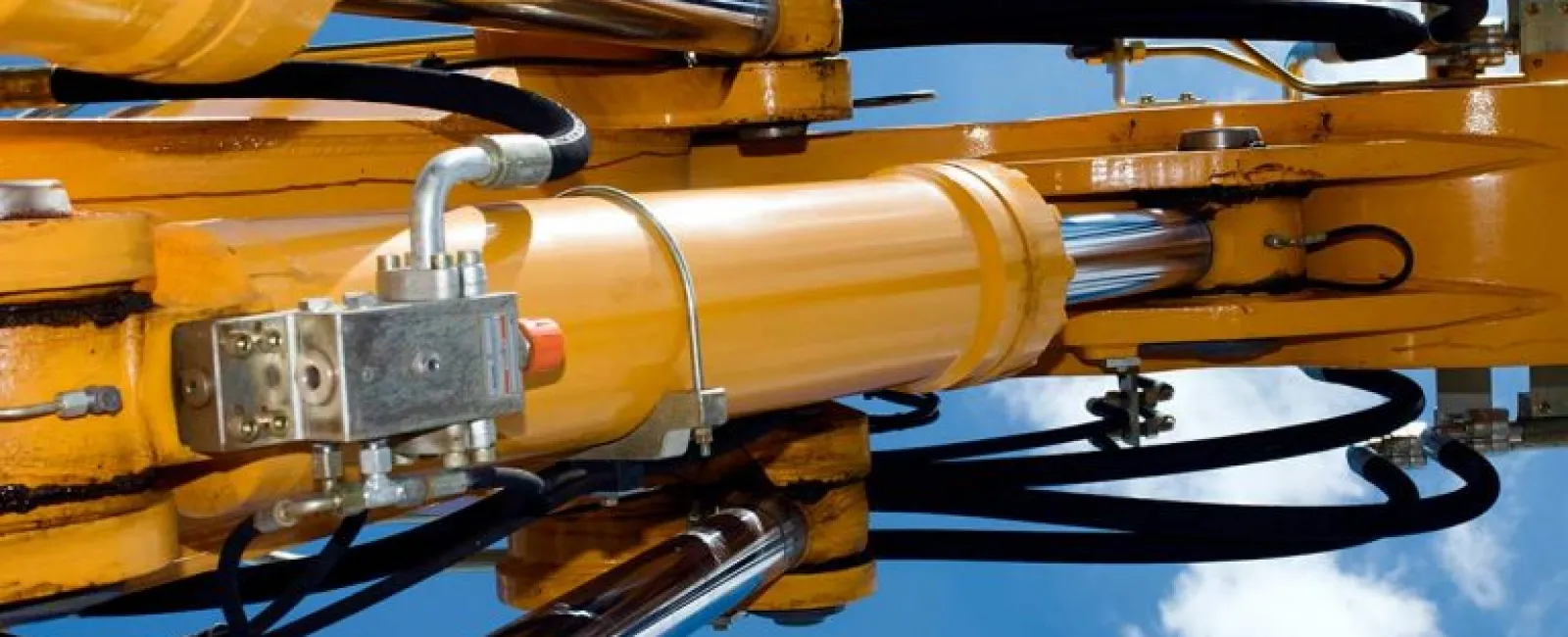 Close-up of yellow hydraulic machinery cylinders and pistons against a clear blue sky with clouds.