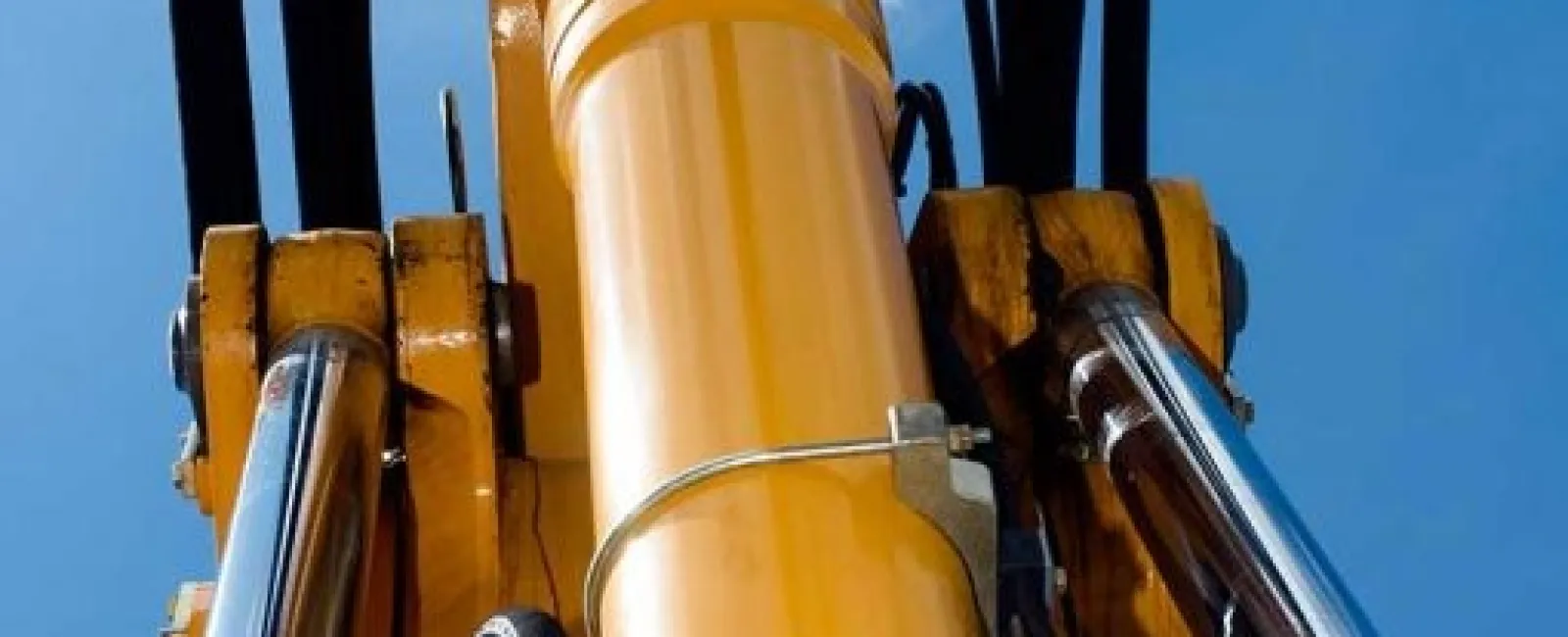 Close-up of yellow hydraulic machinery cylinders and pistons against a clear blue sky with clouds.