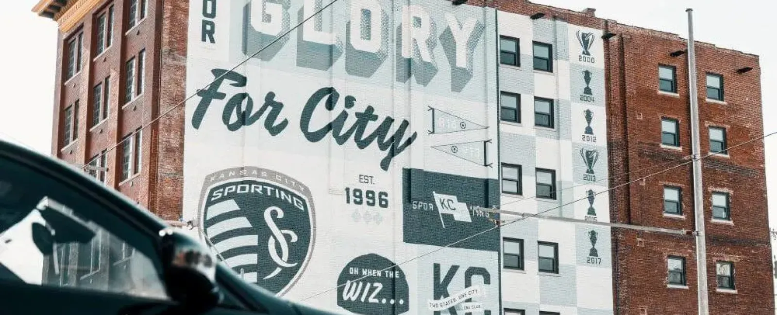Sporting Kansas City mural on brick building celebrating soccer achievements and city pride with trophies and logos.