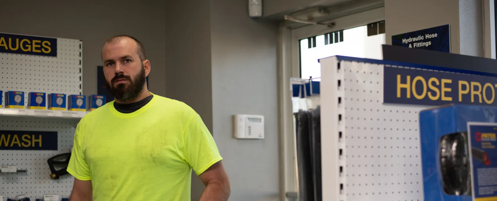 Worker in neon yellow shirt holding a hydraulic hose inside a hose and fittings store with shelves of products
