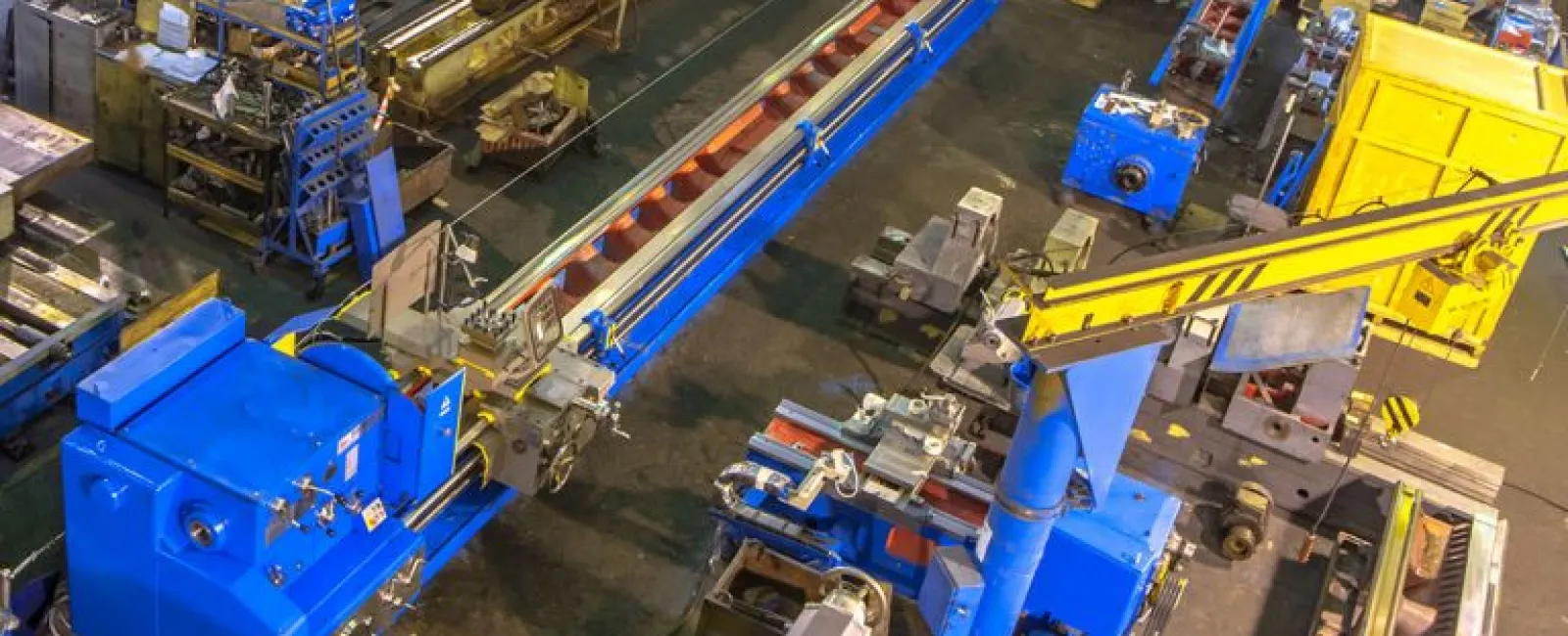 A large industrial workshop with blue machinery, yellow crane, and organized metalworking equipment.
