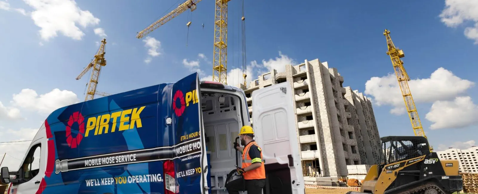 Construction site with cranes, a worker in safety gear accessing a PIRTEK service van under a blue sky.