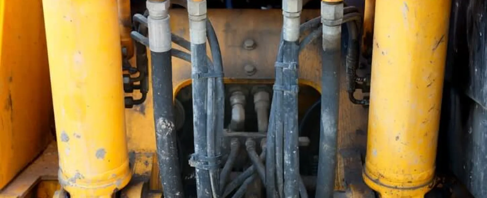 Close-up of yellow heavy machinery hydraulic system with hoses and metal connectors showing wear and dirt