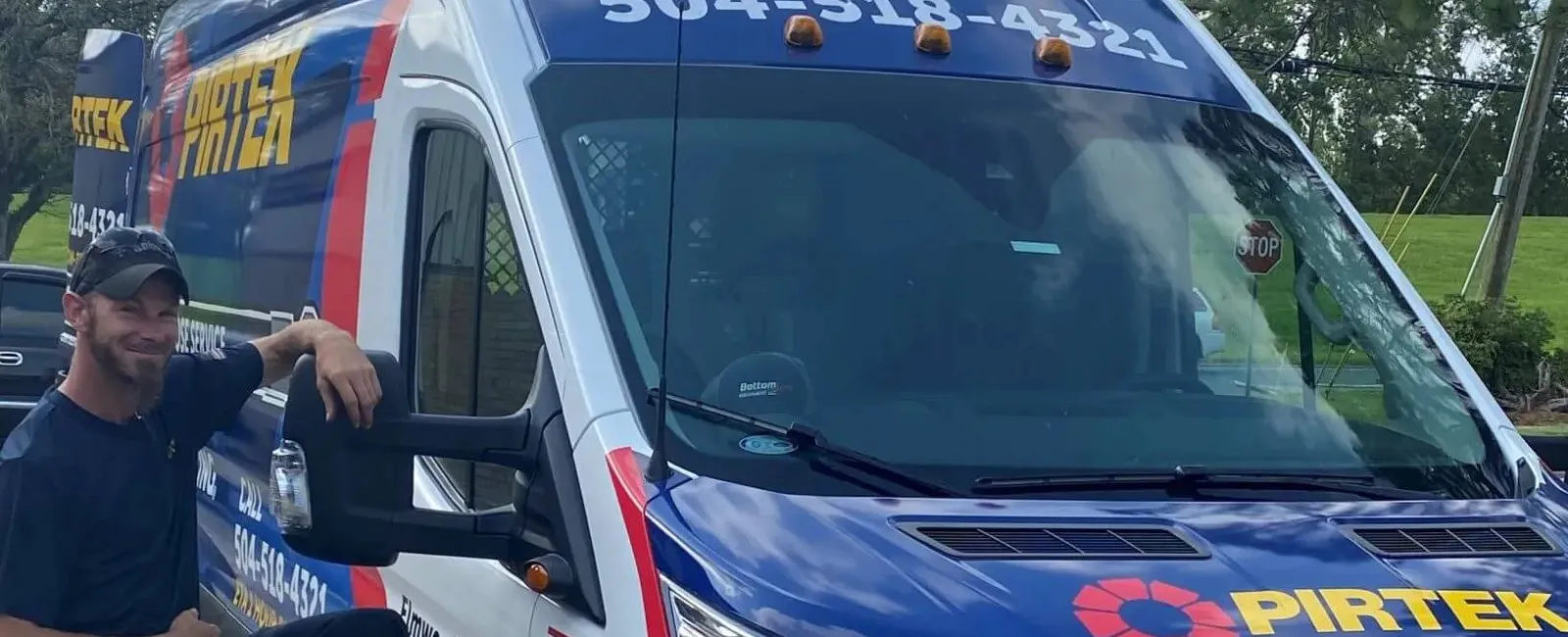 Man posing next to a blue and white Pirtek service van with company logo and contact number visible.