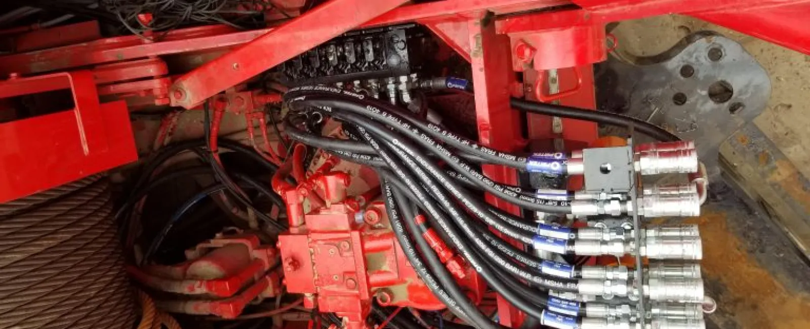 Close-up of hydraulic system with multiple hoses and metal fittings on industrial red machinery.