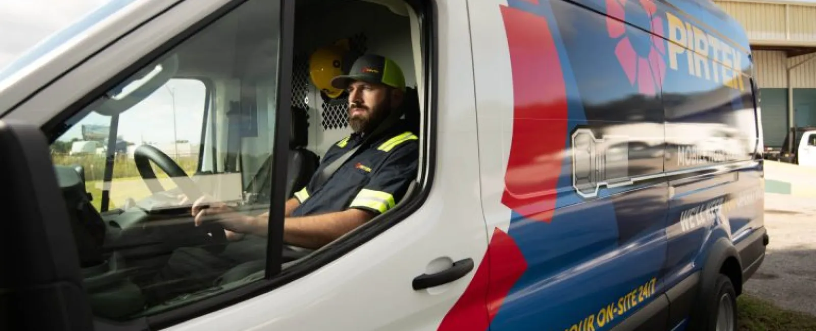 Man in uniform sitting inside a branded service van parked outdoors near a building.