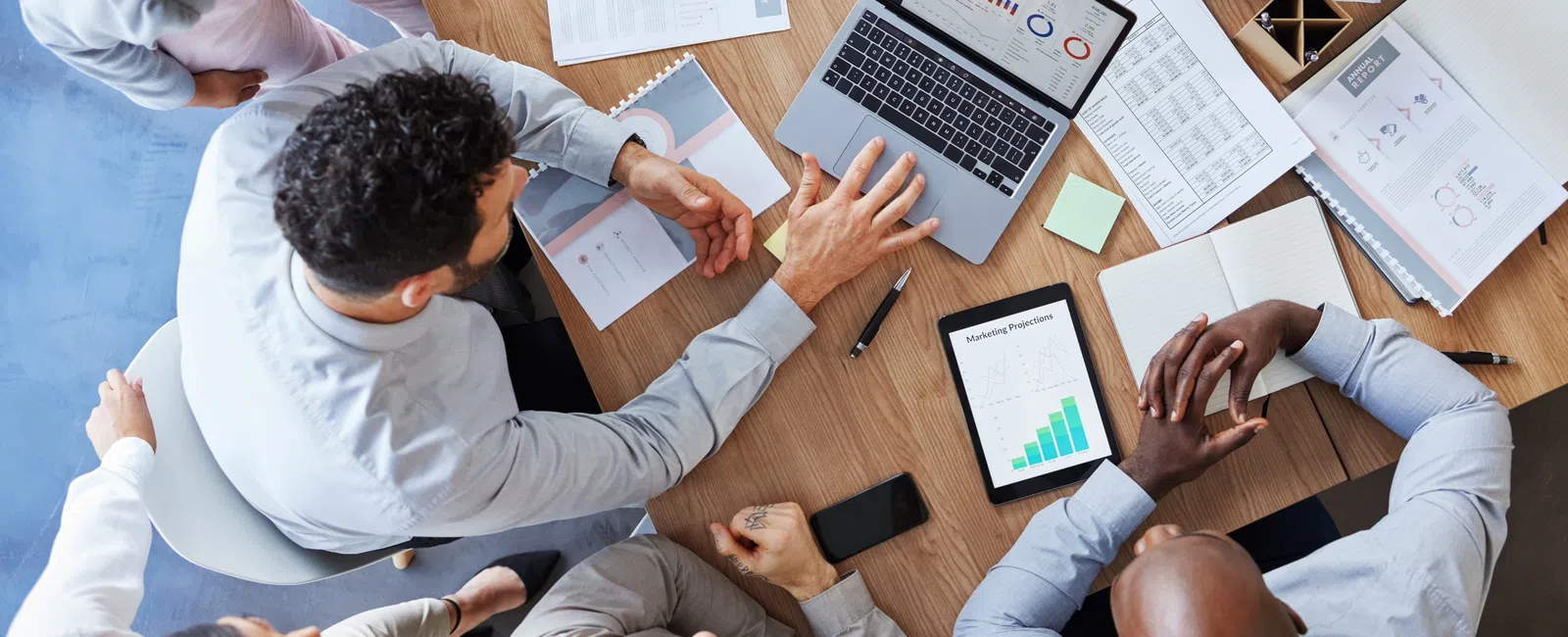 Overhead view of diverse team collaborating at a wooden table with laptops, charts, and coffee during a business meeting