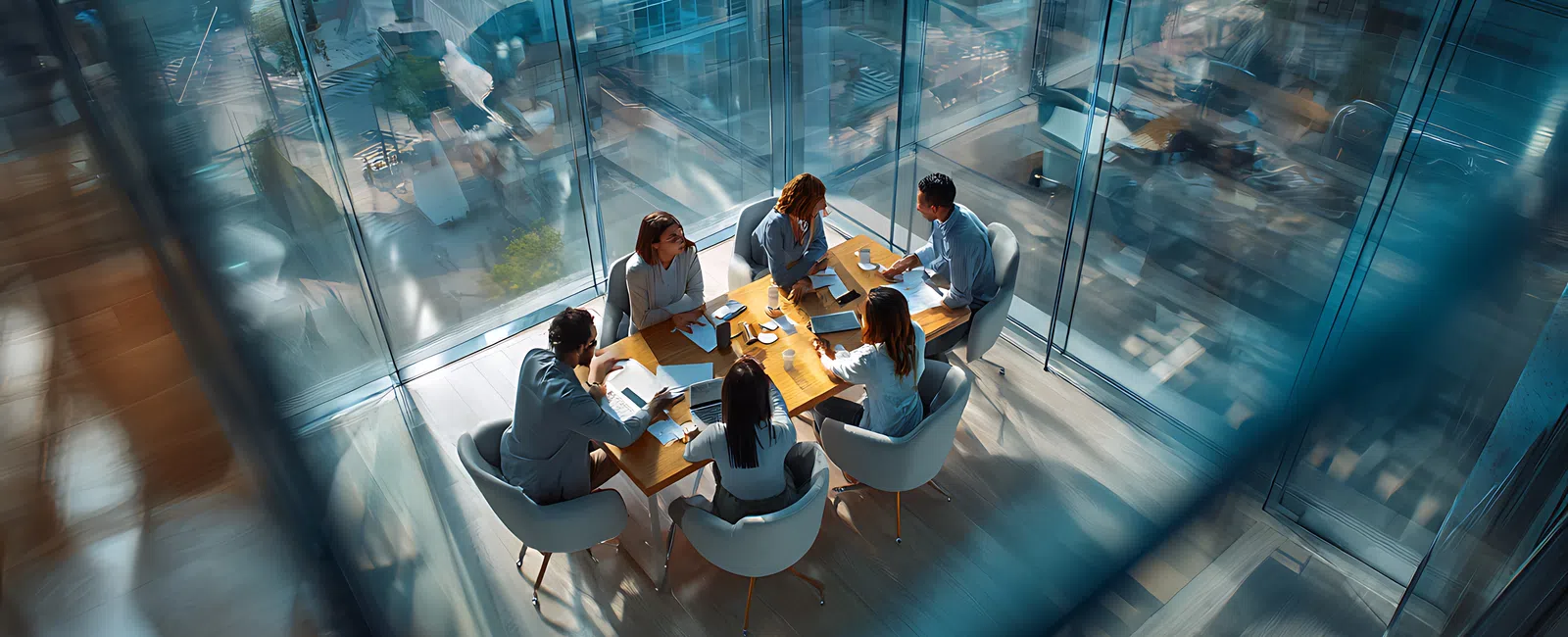Business team of six having a meeting around a wooden table in a glass office with city views.