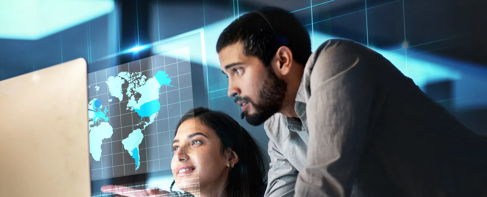 Two professionals analyzing digital data and world map on transparent futuristic screen in office.