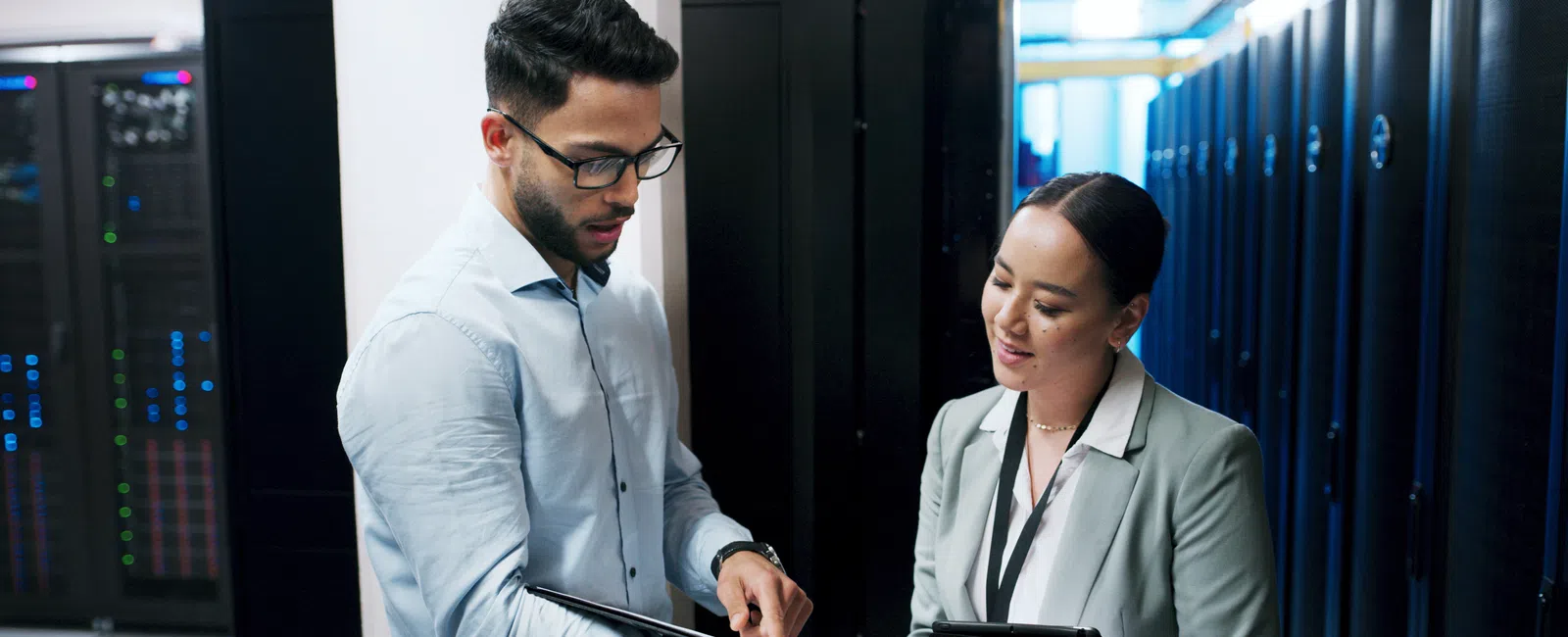 IT professionals discussing data with digital tablets in a server room filled with racks and equipment.