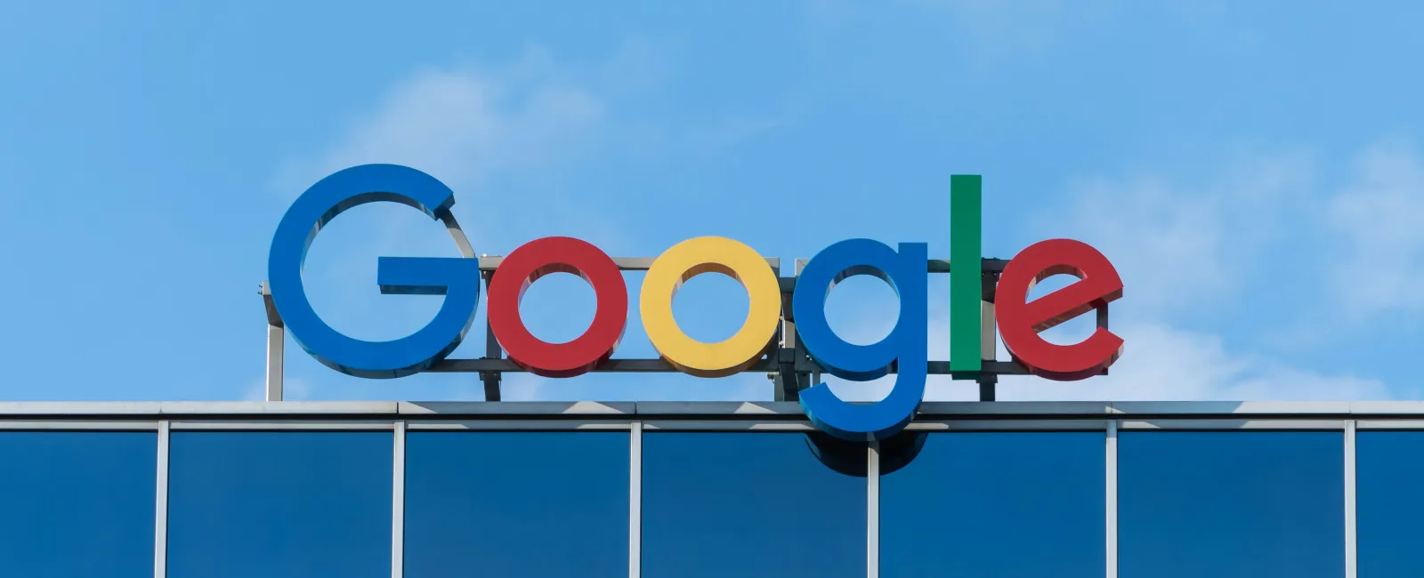 Colorful Google logo sign mounted on top of a building against a clear blue sky.