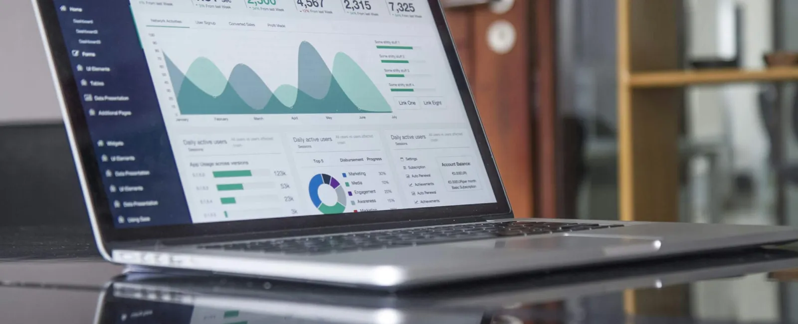 Laptop displaying data analytics dashboard with charts and key statistics on a reflective black table.