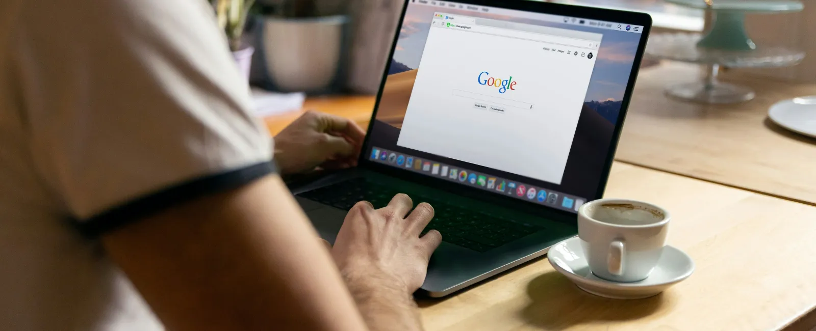 Person using a laptop at a wooden table with Google search open and a cup of coffee nearby