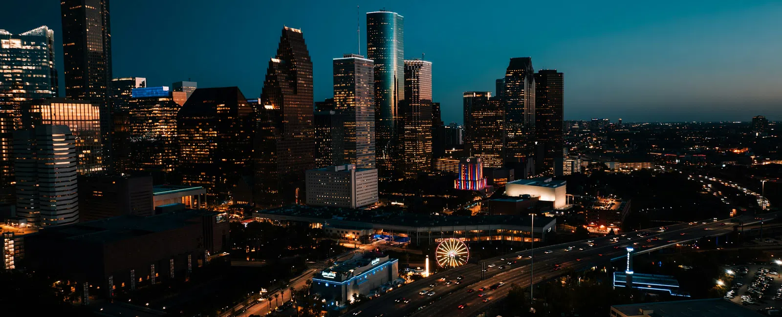 Nighttime cityscape of a modern urban skyline with illuminated skyscrapers and busy highways in Houston.