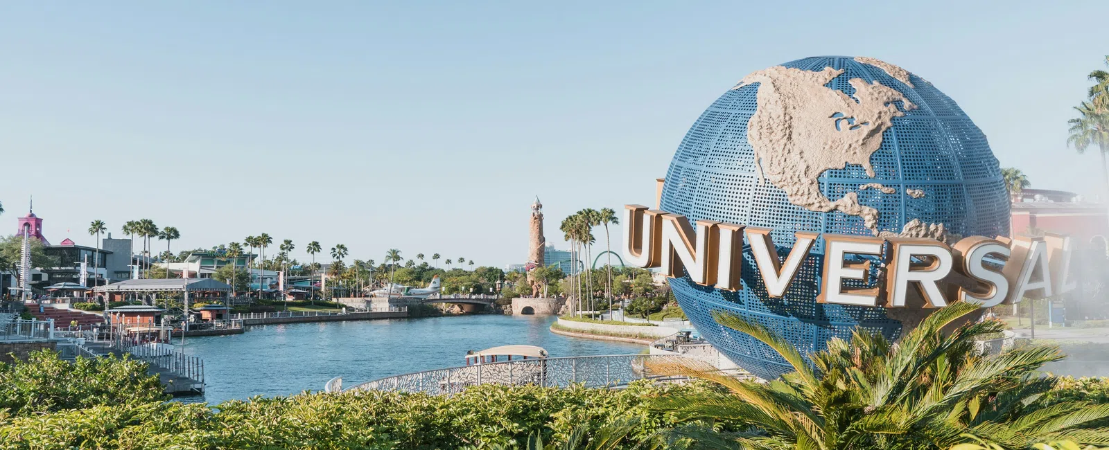 Universal Studios globe sculpture with water and greenery under clear blue sky at theme park entrance.
