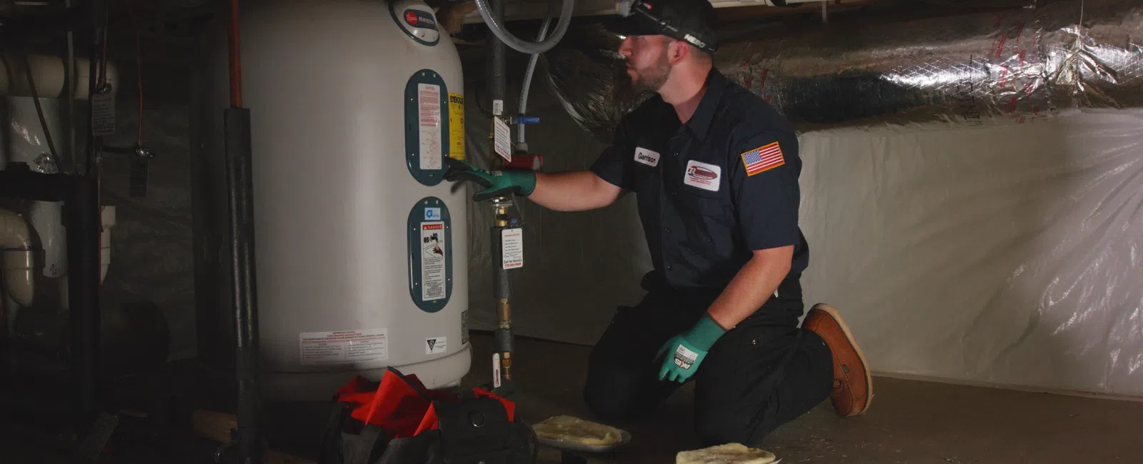 Technician performing maintenance on a water heater in a dimly lit basement.