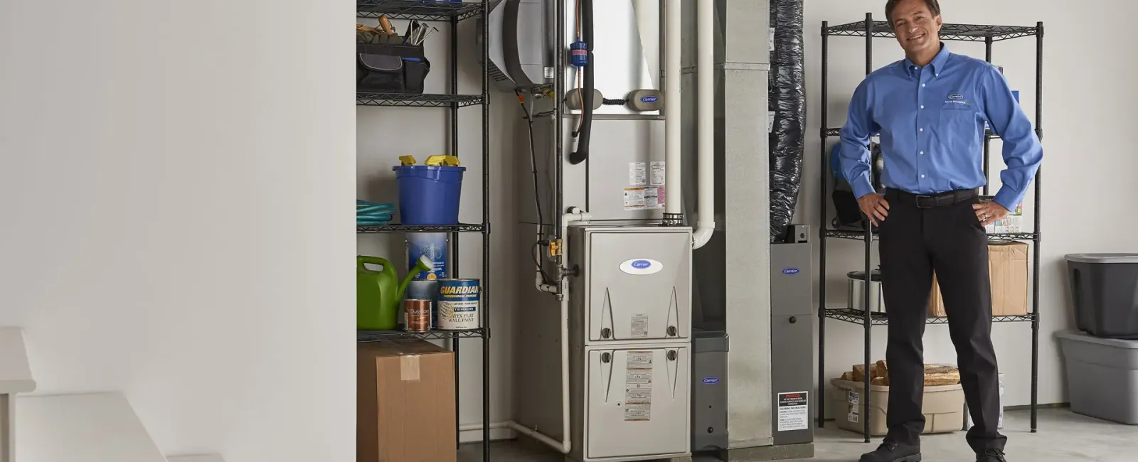 Technician standing in a clean utility room with a modern HVAC furnace and organized storage shelves.