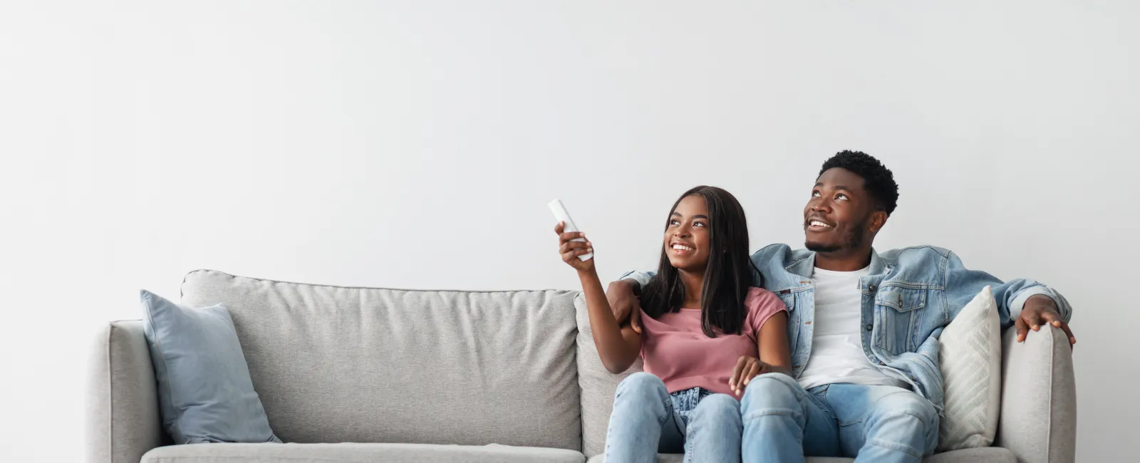 Happy young couple sitting on modern gray sofa watching TV together in a bright minimalist living room