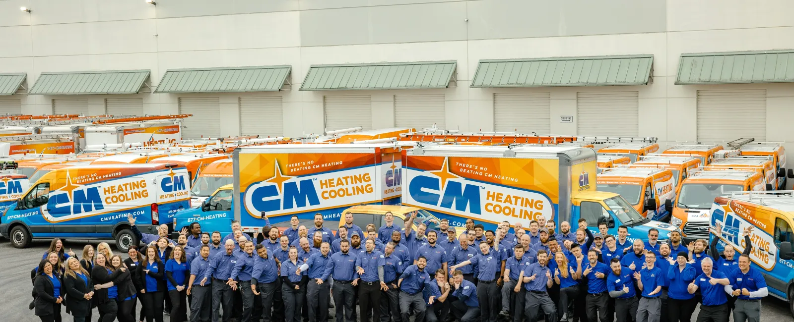 Group photo of CM Heating and Cooling employees standing in front of company service vans with branded logos.