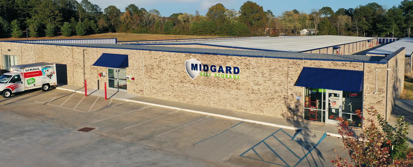 Midgard Self Storage brick building with blue awnings and U-Haul trucks parked outside under a partly cloudy sky.