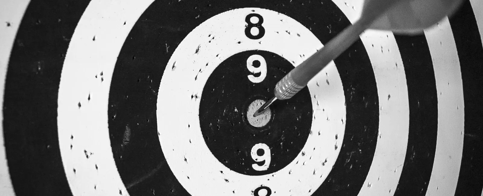 Close-up of a dart perfectly hitting the bullseye on a black and white target board with numbered rings.