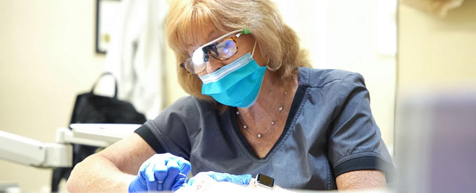 Female medical professional wearing mask and gloves focused on patient care in a bright clinical setting.