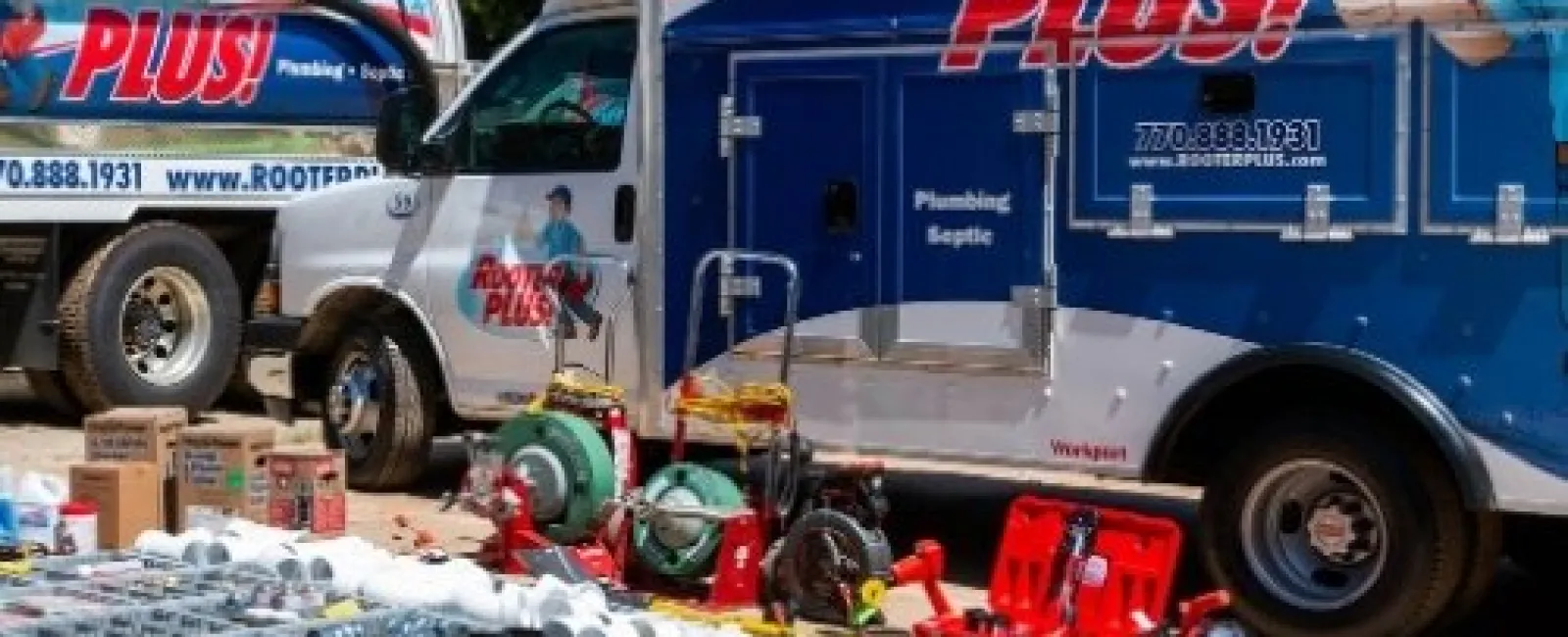 Rooter Plus plumbing trucks with organized plumbing tools and equipment laid out on the ground outdoors.